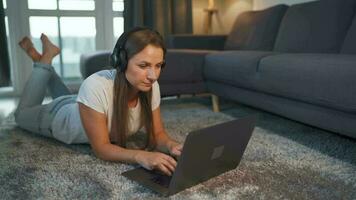 Frau ist Lügen auf das Boden, Arbeiten auf ein Laptop und hört zu zu Musik- auf Kopfhörer. Konzept von Fernbedienung arbeiten. video