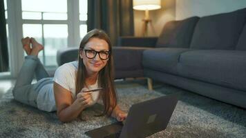 Woman is lying on the floor and and makes an online purchase using a credit card and laptop. Online shopping, lifestyle video