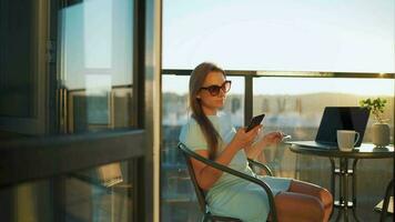 Woman sitting on the balcony against the backdrop of the setting sun and makes an online purchase using a credit card video
