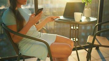 vrouw zittend Aan de balkon tegen de backdrop van de instelling zon en maakt een online aankoop gebruik makend van een credit kaart video