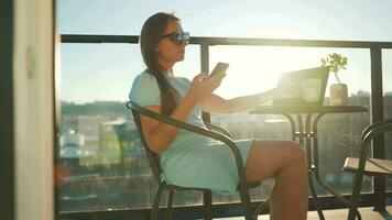 Woman using smartphone on the balcony against the backdrop of the sunset. Outdoor home office. Remote work concept video