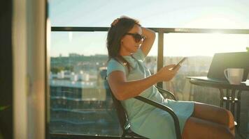 Woman using smartphone on the balcony against the backdrop of the sunset. Outdoor home office. Remote work concept video