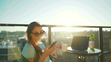 Woman using smartphone on the balcony against the backdrop of the sunset. Outdoor home office. Remote work concept video