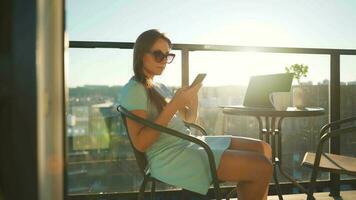 Frau mit Smartphone auf das Balkon gegen das Hintergrund von das Sonnenuntergang. draussen Zuhause Büro. Fernbedienung Arbeit Konzept video