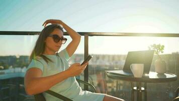 Woman using smartphone on the balcony against the backdrop of the sunset. Outdoor home office. Remote work concept video