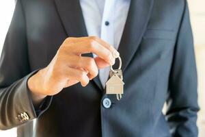 Home agent, broker man in suit standing, realtor holding the house key to hand over to new homeowner or tenant , client after the bank approved the home loan, mortgage loan. Property lease of landlord photo