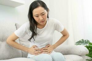 Flatulence asian young woman, girl hand in stomach ache, suffer from food poisoning, abdominal pain and colon problem, gastritis or diarrhoea. Patient belly, abdomen or inflammation, concept. photo