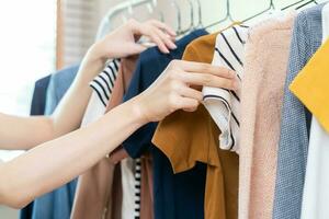 elección de ropa, nada a vestir asiático joven mujer, niña mano en elegir vestido, atuendo en percha en guardarropa en habitación armario a hogar. decidiendo qué a poner en cuales uno. foto