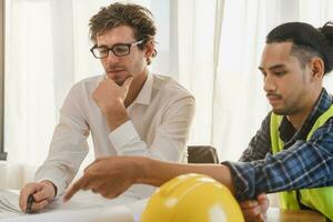 Builder team, hand of asian, caucasian young engineer, architect two man are discussing construction drawing on blueprint follow project to build an industrial plan at site. Engineering worker people. photo