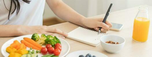 Diet, Dieting hand of woman write diet plan right nutrition on table with fresh vegetables salad, almond is different food ingredients in the green. Nutritionist of healthy, nutrition of weight loss. photo