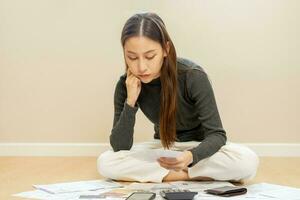 Financial owe asian woman, female sitting on floor home, stressed and confused by calculate expense from invoice or bill, have no money to pay, mortgage or loan. Debt, bankruptcy or bankrupt concept. photo