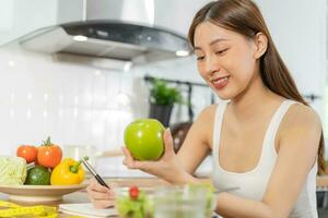 dieta, dieta asiático joven mujer laboral, escribir dieta plan Derecha nutrición, sostener verde manzana, vegetales ensalada es comida para bueno salud no escoger comer basura alimento. nutricionista femenino, peso pérdida persona. foto