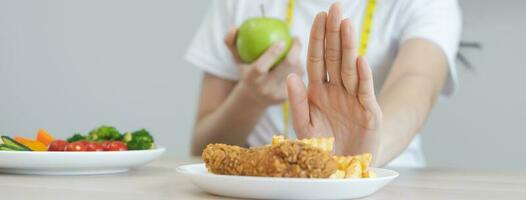 dieta, dieta asiático joven mujer mano en empujar afuera, negar frito pollo, francés frito y escoger verde manzana, vegetales ensalada, comer comida para bueno saludable, salud cuando hambriento. hembra peso pérdida gente. foto