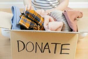 Recycling, Donation for poor, asian young woman, girl sitting pack on floor at home, put on stuff into donate box with second hand clothes, charity helping and needy people. Reuse recycle, moving. photo