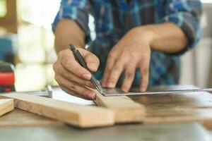 Carpentry professional, hand of asian young man, male carpenter use ruler measure, tool on board wood in small shop. Woodwork, furniture making, construction industry. Owner small business people. photo