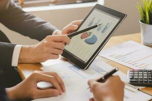 Business meeting, two caucasian, asian group man use tablet brainstorm analyzing on graph data of cost plan or document, paperwork and discussing in board room on table. People working conference room photo