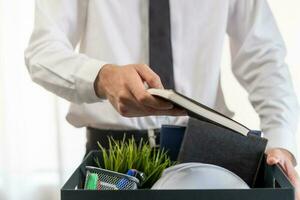 Unemployed, quite job. Desperate caucasian young businessman resigning from company, hand holding stuffs into the cardboard, packing belongings, layoff or changing work. Resignation,employment concept photo