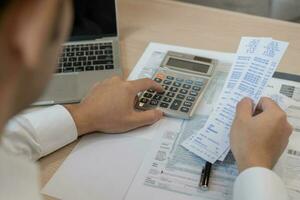 Close up hand of stress asian young businessman, male pressing a calculator to calculate tax income and expenses, bills, credit card for payment or payday at home, office.Financial, finance concept. photo