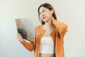 Suffering summer heat stroke, hot weather, tired asian young woman, girl sweaty and thirsty, refreshing with hand in blowing, wave fan to ventilation when temperature high at home, house.on background photo
