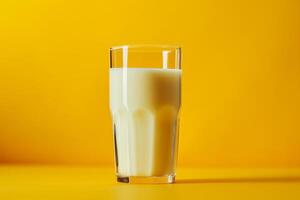 A glass of milk sitting on top of a table in front of a yelow background, photo