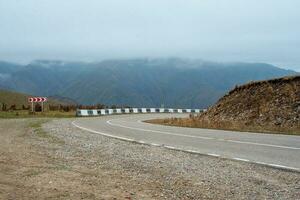 Empty morning highway through the pass, right turn . Beautiful asphalt freeway, motorway, highway through of caucasian landscape mountains hills at cold foggy weather in mid october. photo