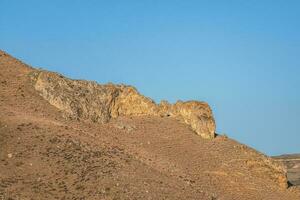 A rock of bizarre shape in a desert landscape against a blue sky. photo