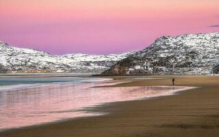 un silueta, un figura en un playa. increíble amanecer polar paisaje con blanco Nevado montaña rango en el horizonte. foto