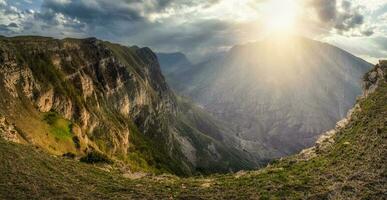 Dramatic scenery with the bright rays of the sun through the clouds over the mountains. Scenic caucasian green landscape with mountain river in deep gorge under overcast sky. photo