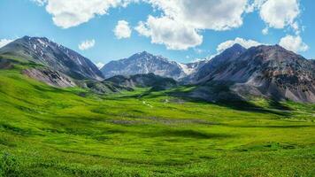 Scenic green blue alpine panoramic landscape with highland valley in sunlight and big glacier under blue cloudy sky. Shadow of clouds on green mountain valley photo