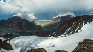 lleno arco iris terminado un glacial montaña valle.atmosferico alpino paisaje con Nevado montañas con arco iris en lluvioso y soleado clima. foto