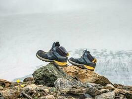 Wet hiking boots dry on a stone against the background of snow-covered high mountains. The difficulties of hiking, drying clothes in nature. photo