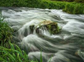 Nature background with boulders in water riffle of mountain river. Powerful water stream of mountain creek. Backdrop of fast flow of mountain brook with rapids photo