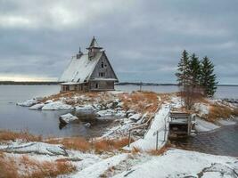 Snowy winter landscape with authentic cinematic house on the shore in the Russian village Rabocheostrovsk. photo