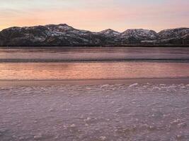 Natural sunset background. An ice-covered mountain lake. Magic pink sunset on a mountain North of the lake. photo