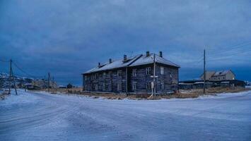 The blue hour. Vintage houses on the background of snow-covered Arctic hills. Old authentic village of Teriberka. photo