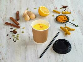 Golden milk in a paper cup with turmeric, cinnamon,ginger, lemon and pepper. Prevention of antiviral infections photo