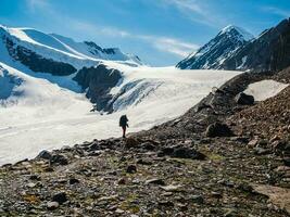 solo trekking en el montañas. un masculino caminantes abajo el montaña camino. en el fondo, grande nevadas montañas. foto