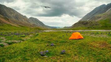 Panoramic view of the camping on the summer green high-altitude plateau. An orange tent on a rainy day. Peace and relaxation in any weather in nature. photo