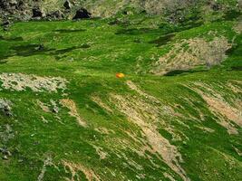 Minimalistic landscape of a green mountain slope with a small tent. Scenic alpine landscape with tent on green hill among rocks. photo