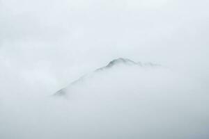 Soft focus. Wonderful minimalist landscape with big snowy mountain peaks above low clouds. Atmospheric minimalism with large snow mountain tops in cloudy sky. photo