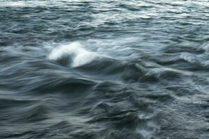 The stream of water, blurred view. Powerful water flow with breakers on the sea photo