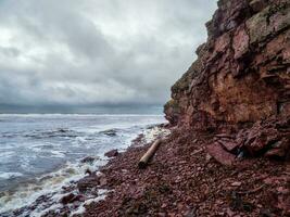 A cliff above the sea with a narrow coastline. Waves with white foam roll on the rocky shore. Tersky coast photo