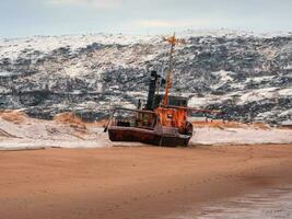 An old rusty fishing boat abandoned by a storm on the shore. Graveyard of ships, old fishing village on the shore of the Barents sea, the Kola Peninsula photo