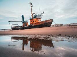 An old rusty fishing boat washed up on a sandy beach in the Barents Sea. Authentic the North sea. photo