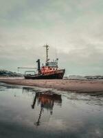An old rusty fishing boat washed up on a sandy beach in the Barents Sea. Authentic the North sea. Teriberka. photo