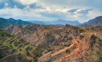 montaña gradas. un rocoso repisa extensión dentro el distancia en contra el antecedentes de rojo texturizado montañas cubierto con escaso vegetación. panorámico vista. foto