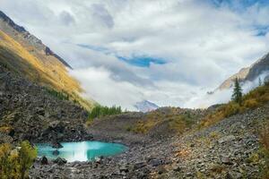 Panoramic view of the autumn mountain, fog over the mountain slopes in the distance, white clouds filling the mountain gorge. A clear blue mountain lake and a bright autumn forest. photo