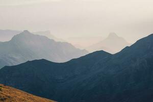 Scenic dawn mountain landscape with light fog in valley among mountains silhouettes under cloudy sky. Vivid sunset or sunrise scenery with low clouds in mountain valley in soft color. photo