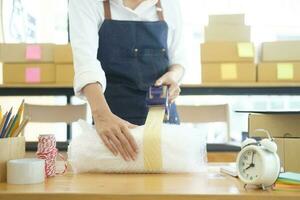 Asian female clothes shop owner folding a t-shirt and packing in a cardboard parcel box. photo