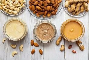 Jars of almond, cashew and peanut butter on white wooden table. Organic, homemade nut butter for wellness breakfast. photo